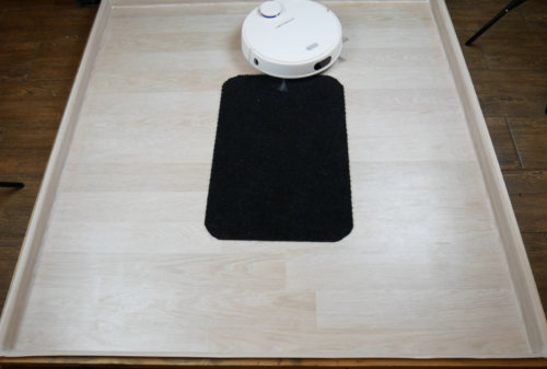 Robotas dulkių siurblys ir juodas kilimėlis